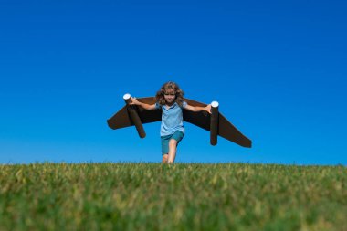 Mutlu çocuk dışarıda yeşil çimlerde ve mavi gökyüzünde oynuyor. Oyuncak jetpack 'li çocuk pilot. Çocuk oyuncak uçak kartonuyla oynuyor. Yaz seyahati ve macera. Başarı, hayal gücü ve rüya konsepti.