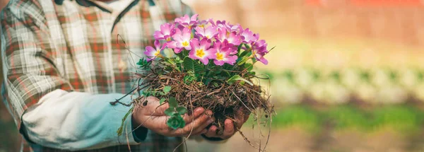 Frühlingsbanner. Kind arbeitet im Garten in der Nähe von Blumengarten. Jungbauer. Junge in Gummistiefeln spielt auf Frühlingswiese. — Stockfoto