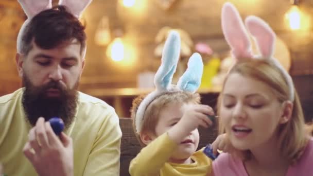 Wielkanocna rodzina matki, ojca i dziecka malowała jajka, nosząc królicze uszy w Wielkanoc. — Wideo stockowe