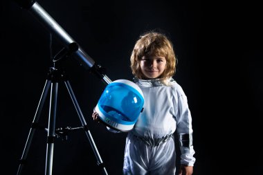 Astronot başlığı ve teleskop takan küçük bir çocuk. Astronotun içinde oynayan ve uzay adamı olmayı hayal eden sevimli bir çocuk. Astronomi ve astroloji kavramı.