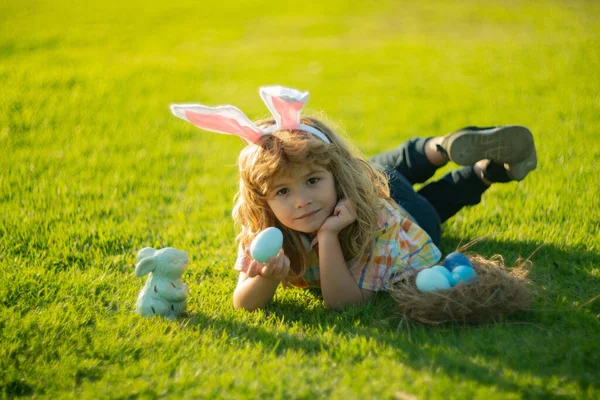 Rapaz caçar ovo no dia de Páscoa ao ar livre. Crianças coelho da Páscoa ovos de caça que colocam na grama no parque, usar orelhas de coelho. Primavera férias em família. — Fotografia de Stock