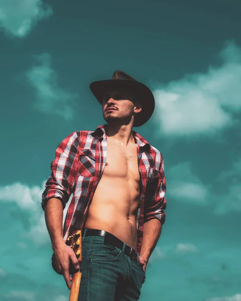 Costura de vaquero. Retrato de un joven con sombrero de vaquero y mirando hacia arriba mientras está de pie sobre el fondo del cielo. Joven de moda. Chico guapo con cara confiada. — Foto de Stock
