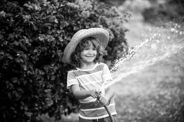 Vicces kisfiú, aki kerti slaggal játszik az udvaron. A gyerek szórakozik a vízpermettel. Nyári szabadtéri tevékenység gyerekeknek. — Stock Fotó