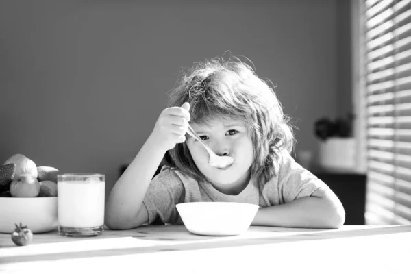 Portret van een kind dat soep eet of ontbijt. Kind met een lepel en een bord in de keuken thuis. — Stockfoto