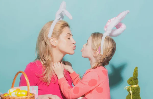 Szczęśliwa rodzina przygotowuje się do Wielkanocy. Słodka dziewczynka i mama w króliczych uszach. Mama i córka całują się. — Zdjęcie stockowe