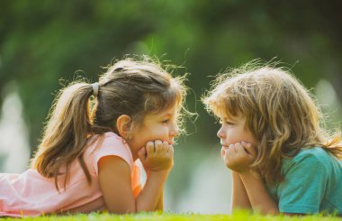 Erkek ve kız kardeş parkta eğleniyor, iki neşeli çocuk yeşil çimlere uzanıyor. Mutlu aile aşkı ve mutluluk kavramı.