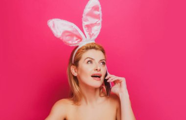 Paskalya tavşanı. Pembe arka planda cep telefonu olan şok olmuş genç bir kadının portresi..