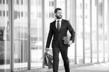 İş adamı alışveriş merkezinde alışveriş yapıyor. Takım elbiseli mutlu iş adamı elinde kağıt torbalarla. Alışverişi seven adam.