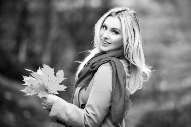 Parlak kırmızı örtülü ve sıcak eşarp takan bir kız. Sarışın ve melek güzelinin yakın portresi. Parkta yürüyen sonbahar kraliçesi. Düşen sarı yaprakları tutan bir kadın..