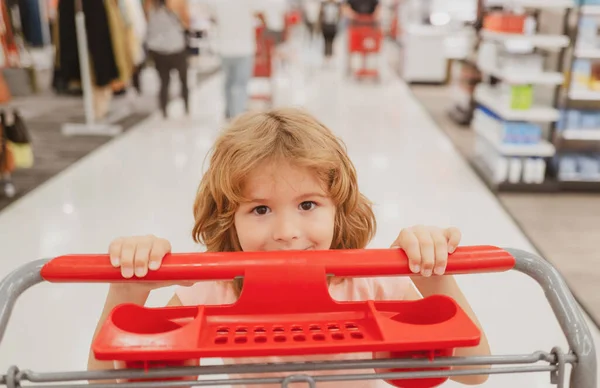 Ritratto ravvicinato di bambino con carrello della spesa che acquista cibo in un negozio di alimentari. Clienti famiglia acquistare prodotti al supermercato. Faccia divertente per bambini. — Foto Stock