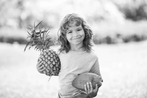 Kind met ananas en kokosnoot die glimlacht met een vrolijk gezicht. Zomervruchten. — Stockfoto
