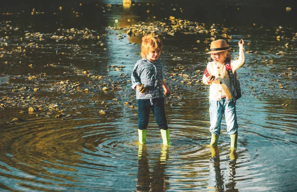 Los niños tiran piedras al río Stony. Hermosos niños lanzan una roca al río. Saltar rocas. — Foto de Stock