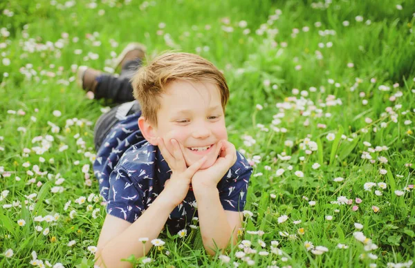 En bekymmerslös, leende pojke på blomsterfältet. Söt unge barn njuter på gräsmattan och drömmer. — Stockfoto