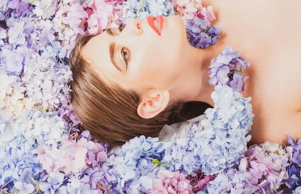 Piękna kobieta leżąca na kwiatach. Kosmetyki do makijażu i pielęgnacji skóry. Dziewczyna z hortensji kwiaty. — Zdjęcie stockowe