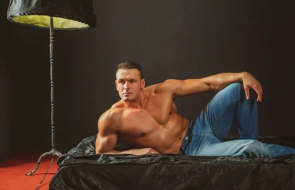 Retrato jovem sexy homens fisiculturista atleta, com um tronco nu, encontra-se em uma cama em travesseiros em roupa interior. — Fotografia de Stock