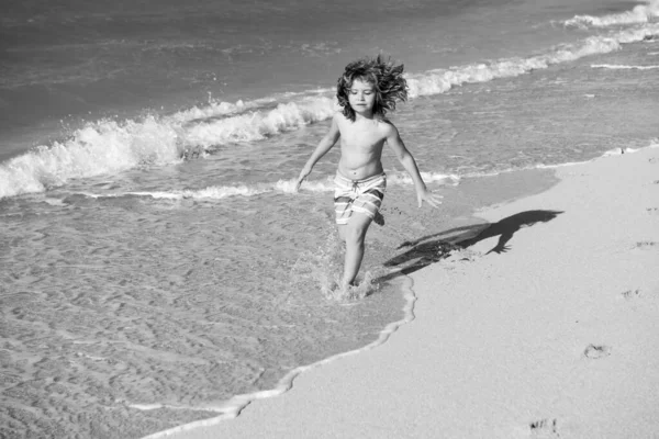Ragazzo felice divertirsi sulla spiaggia tropicale del mare. Bambino divertente correre con spruzzi di acqua piscina lungo il bordo surf. Attività per bambini durante le vacanze estive. — Foto Stock