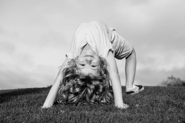 Happy child standing upside down on green grass. Laughing kid boy having fun in spring park. Healthy kids lifestyle concept. — Stock Photo, Image