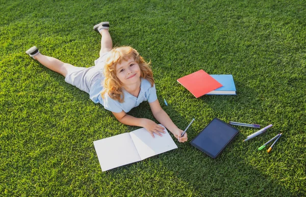 Portrait d'enfant garçon heureux avec écriture de livre sur ordinateur portable dans le parc. L'éducation précoce des enfants. Un gamin a lu un livre dans le jardin. Les devoirs d'été. Étudiant préscolaire en plein air. — Photo