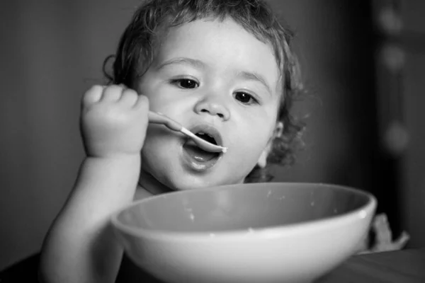Funny little baby in the kitchen eating with fingers from plate. — Stock Photo, Image