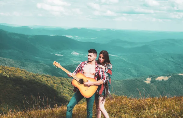 Pohledný hipster muž a ženy odpočívají v horách s kytarou. Krásný výhled na údolí v pozadí. — Stock fotografie