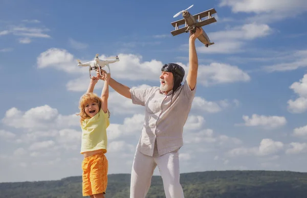 青空と雲の背景の上に飛行機とクワッドコプターのドローンを持つ祖父と息子。子供との高齢者の親戚. — ストック写真