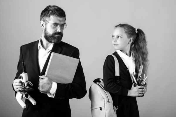 Linda colegiala con profesor en la escuela. Retrato de estudio de tutor y niña con mochila y libro de texto. — Foto de Stock