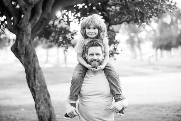 Mutlu baba ve oğul güneşli bir parkta tatilin tadını çıkarıyorlar. Babam omuzlarında mutlu küçük bir çocuk taşıyor.. — Stok fotoğraf