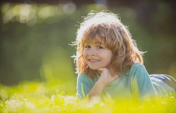 Porträt eines fröhlich lachenden Kindes, das im Sommer im Naturpark auf Gras liegt. Positive Kindergesichter aus der Nähe. — Stockfoto