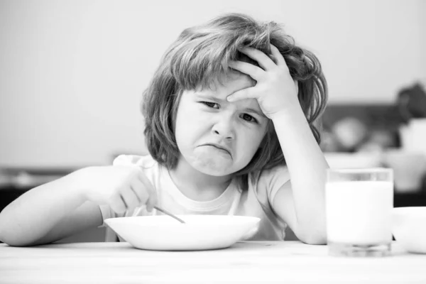 Μη συγκεντρωμένο αγοράκι που τρώει σούπα για μεσημεριανό. Δυσάρεστο Καυκάσιο παιδί κάθεται στο τραπέζι στην κουζίνα του σπιτιού δεν έχει όρεξη. Αναστατωμένο μικρό παιδί αρνείται να φάει βιολογικά δημητριακά με γάλα. — Φωτογραφία Αρχείου