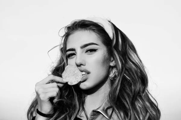 Portrait of young woman, beautiful lips, bright make-up holding, eating fried potato, fries, chips and posing over blue background. Unhealthy eating. Pretty woman eating potato chips, close up. — Stock Photo, Image