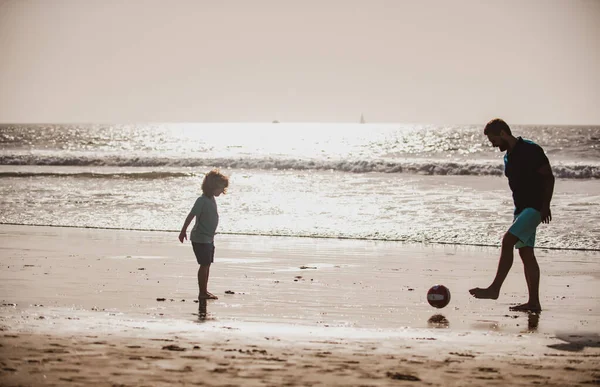 父と息子は夏休みにビーチでサッカーやサッカーをします。日没の屋外シルエットを楽しむお父さんと子供. — ストック写真