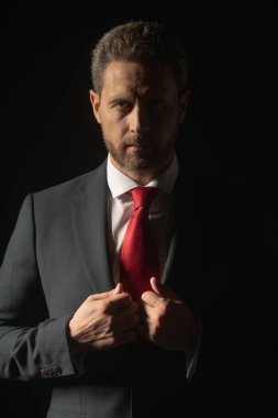 Takım elbiseli ve kravatlı ciddi bir iş adamının stüdyo portresi ve izole edilmiş karanlık arka planda dikilirken düşünceli bir görünüm. Ciddi bir iş adamı yüzü..