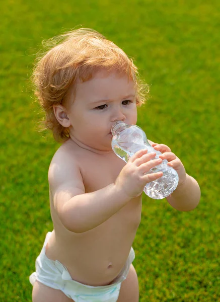 아기 식수. 푸른 잔디가 깔려 있는 병에서 신선하고 순수 한 물을 마시는 금발의 어린 아이의 근접 사진. — 스톡 사진
