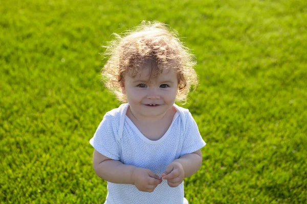 Gelukkige baby in gras op de fieald op zonnige zomeravond. Lachend kind buiten. Baby gezicht close-up. Grappig klein kind close-up portret. Blond kind, lachende emotie gezicht. — Stockfoto