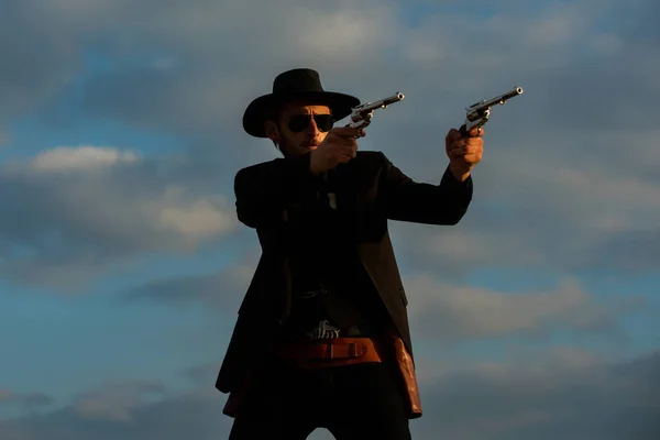 Стрельба в ковбоя. Офицер шерифа в черном костюме и ковбойской шляпе. Человек с пушками Дикого Запада, винтажным пистолетом и боеприпасами маршала. Федеральные маршалы, американский западный шериф. Дикий Запад с ковбоем. — стоковое фото