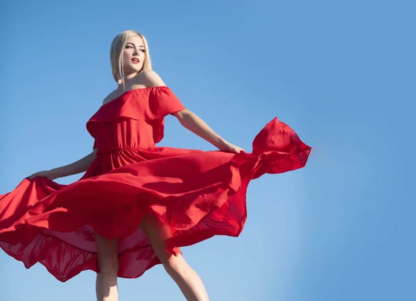 Vrouw in rode jurk beweging aan de hemel. Stijlvolle mode vrouw poseren buiten. Aantrekkelijke jonge vrouw in sexy jurk genieten zomer. — Stockfoto