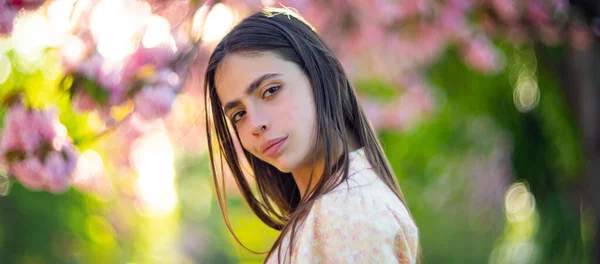 春の女の子の顔。桜の花の背景に優しい女性の肖像画を閉じます。バナー春のデザイン、ウェブサイトのヘッダーの広告. — ストック写真