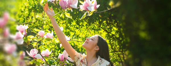 Bahar kadını pankarta karşı. Bahar çiçekleri arka planında genç bir kız. Manolya. Çiçek dallı güzel genç bir kadın, Bahar bahçesindeki genç bir kadın. — Stok fotoğraf