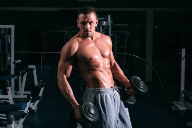 Dambıllar spor salonunda çalışıyor. Dambıllı adam eğitimi. Sağlıklı bir yaşam tarzı. Vücut geliştirme konsepti. Sporcu kasları.