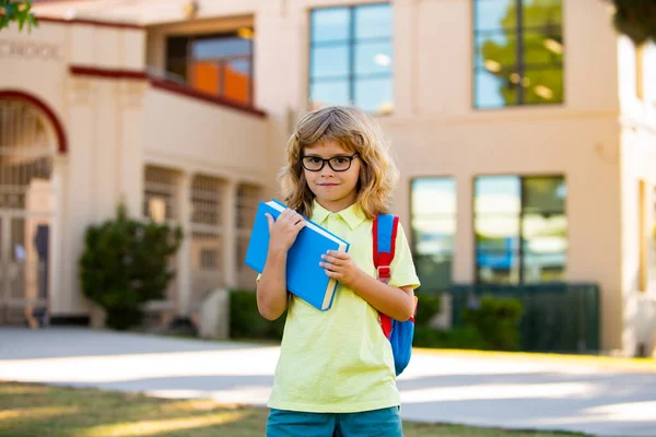 Un gamin de l'école primaire. Happy boy en lunettes va à l'école pour la première fois. Enfant avec cartable et livre. Retour à l'école. — Photo