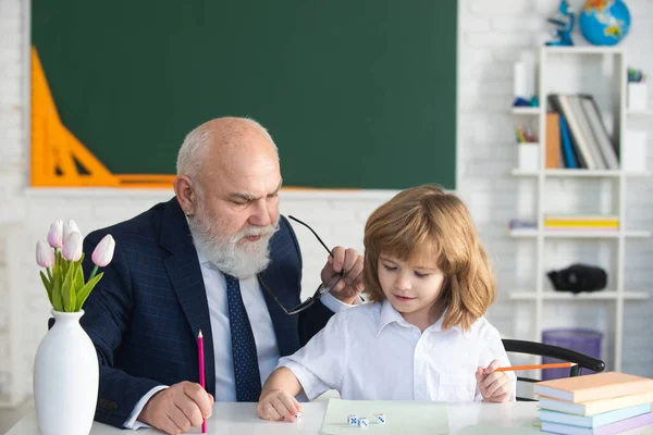 Niño feliz en la escuela. El viejo maestro mayor ayuda a escribir. Educación, docencia, escuela primaria. — Foto de Stock