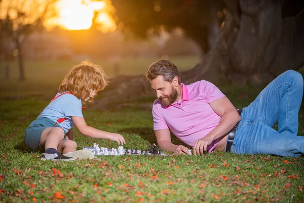 Šťastná rodina venku. Otec a syn hrají šachy na podzimní zahradě. Aktivní lidé baví a hrát šachy v parku, trávit čas s dítětem. — Stock fotografie