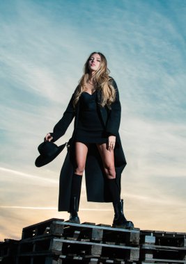 Siyah paltolu, şapkalı ve siyah çizmeli seksi kadın. Moda elbiseli genç bir manken. Yazın moda kadını..