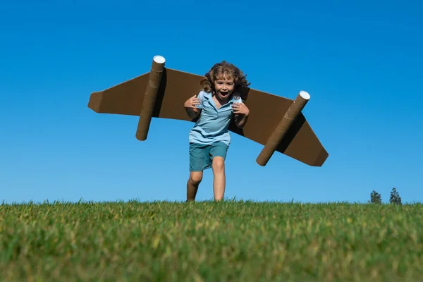 Glada barn leker ute på grönt gräs och blå himmel. Kid pilot med leksak jetpack. Grabben leker med leksakskartong. Sommarresor och äventyr. Framgångsvinnare, fantasi och drömkoncept. — Stockfoto