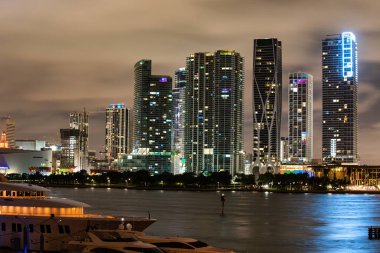 Miami şehir gecesi. Günbatımında Miami Florida, aydınlık binaların ufuk çizgisi ve Macarthur Köprüsü.