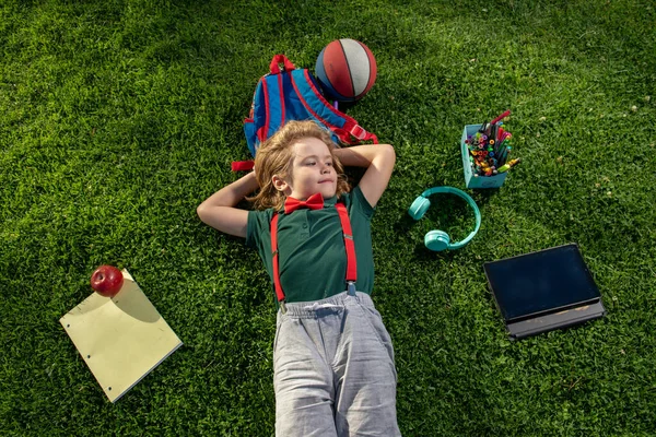 Vue du dessus d'un élève d'âge préscolaire allongé sur l'herbe et prenant un cours à l'extérieur. Garçon heureux relaxant sur l'herbe. — Photo