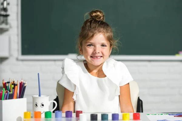 小さな女の子は学校の教室で鉛筆クレヨンでカラフルな絵を描いています。面白い女子高生の顔. — ストック写真