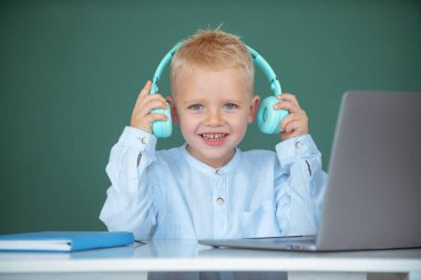 Kulaklıklı akıllı çocuk masada oturur, okulda dizüstü bilgisayarda çalışır, klever çocuk internet derslerini kullanarak öğrenirken kulaklık takar. Bilgi günü.