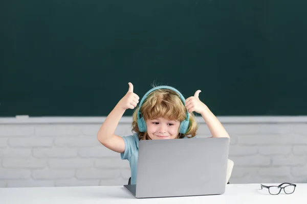 Primeiro dia na escola. Menino com polegares para cima em fones de ouvido usando um laptop e estudar on-line com professor de chamadas de vídeo na escola. — Fotografia de Stock