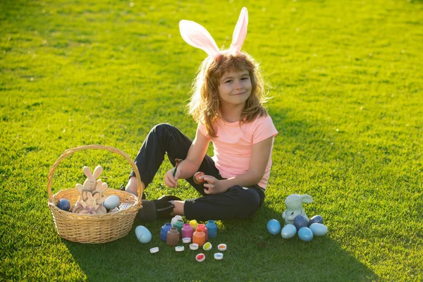 Ребенок с пасхальными яйцами и кроличьими ушами, лежащими на траве. Счастливого Пасхального детского лица. Милый маленький мальчик, пасхальные кролики дети весной на открытом воздухе. — стоковое фото